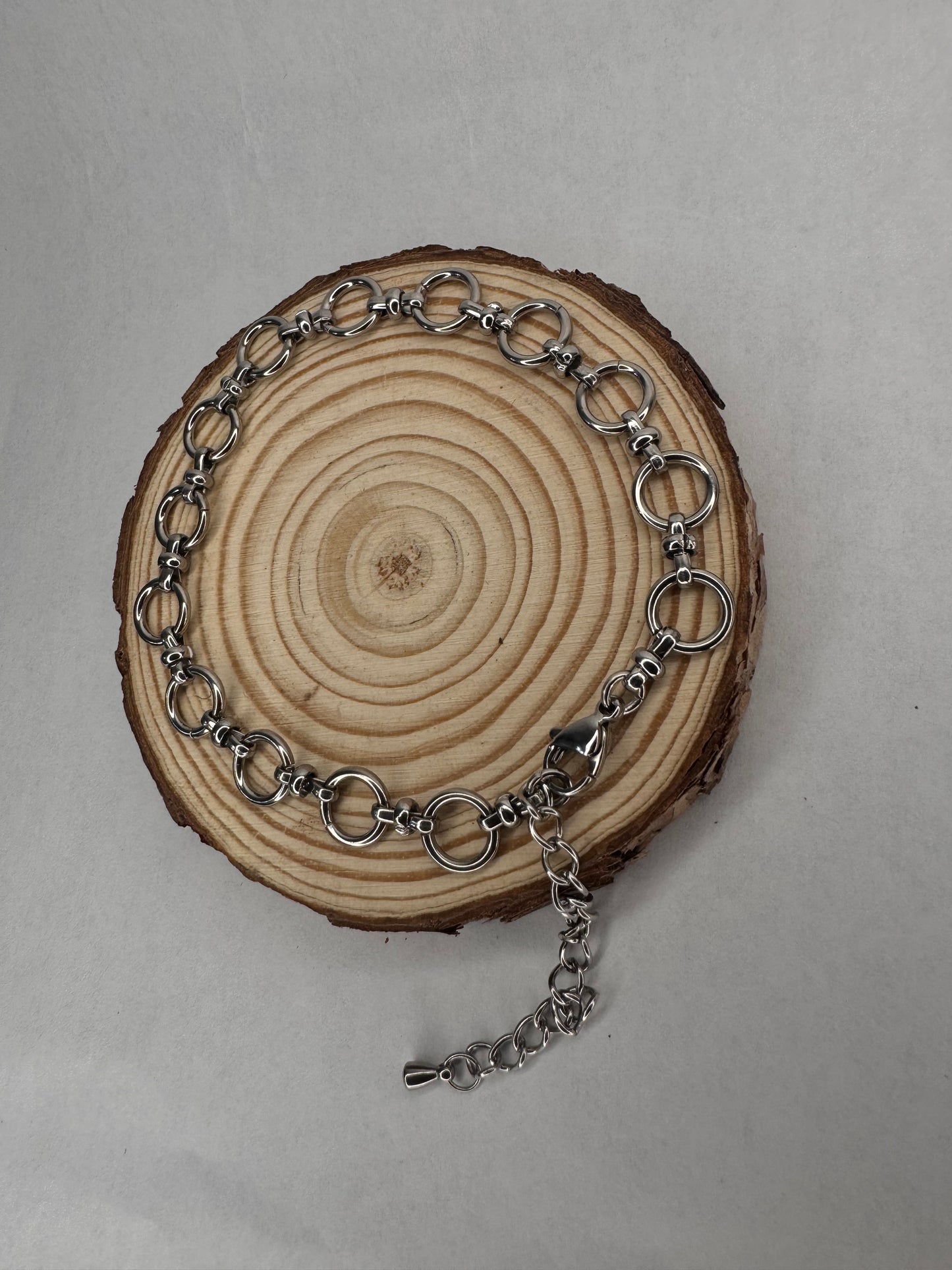 Silver chain anklet  on a wooden circular piece with a plain background