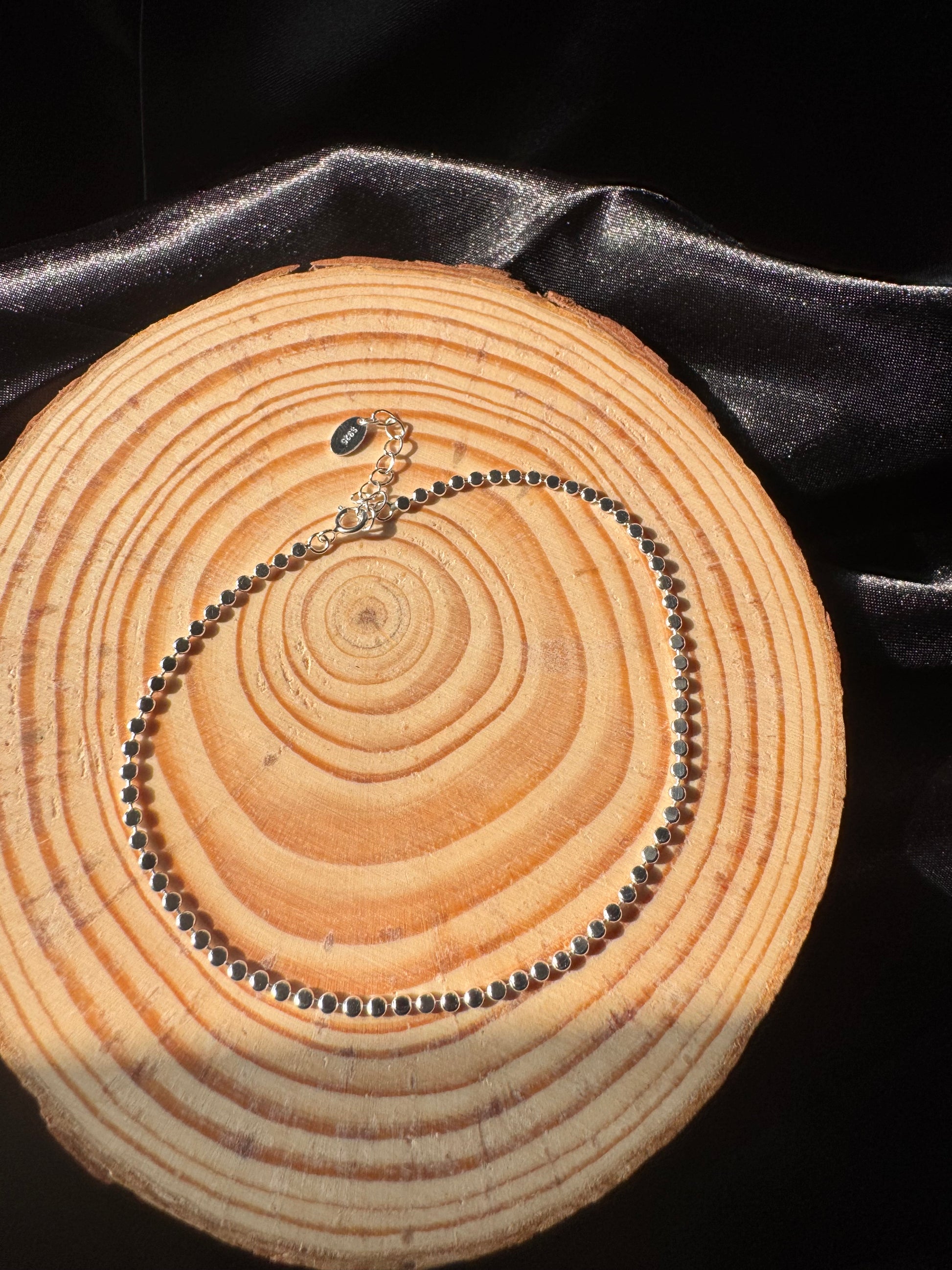 Silver anklet on a wooden surface with black satin fabric