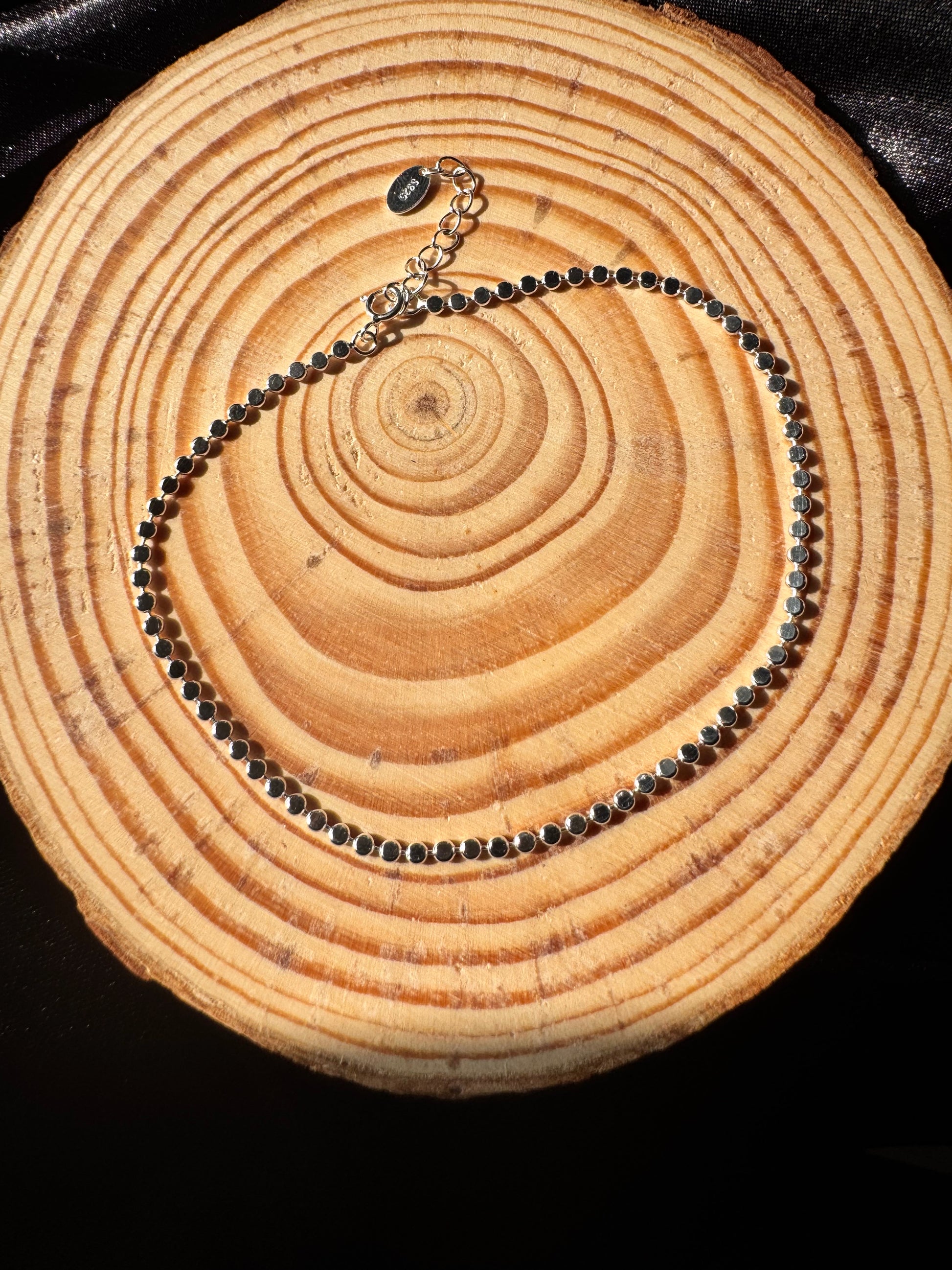 Silver anklet on a wooden surface with visible grain 