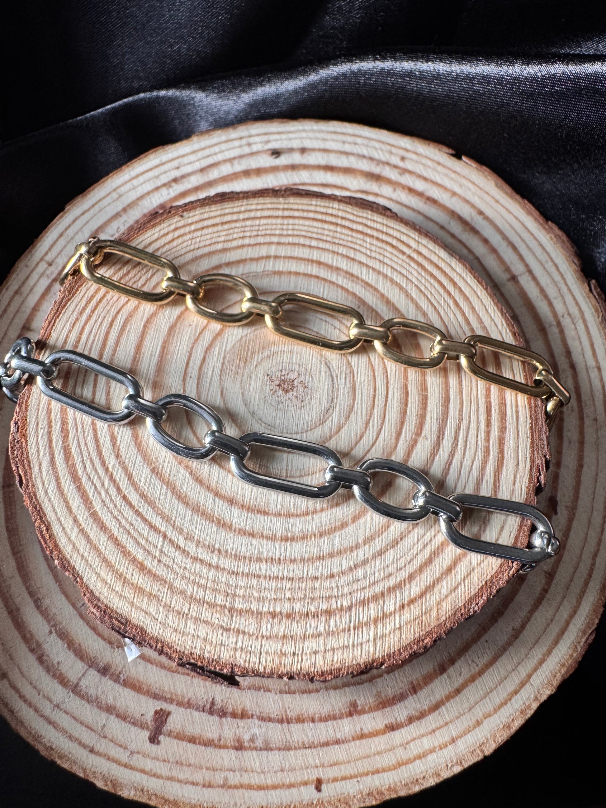 Two chain anklets, one gold and one silver, on a wooden surface.