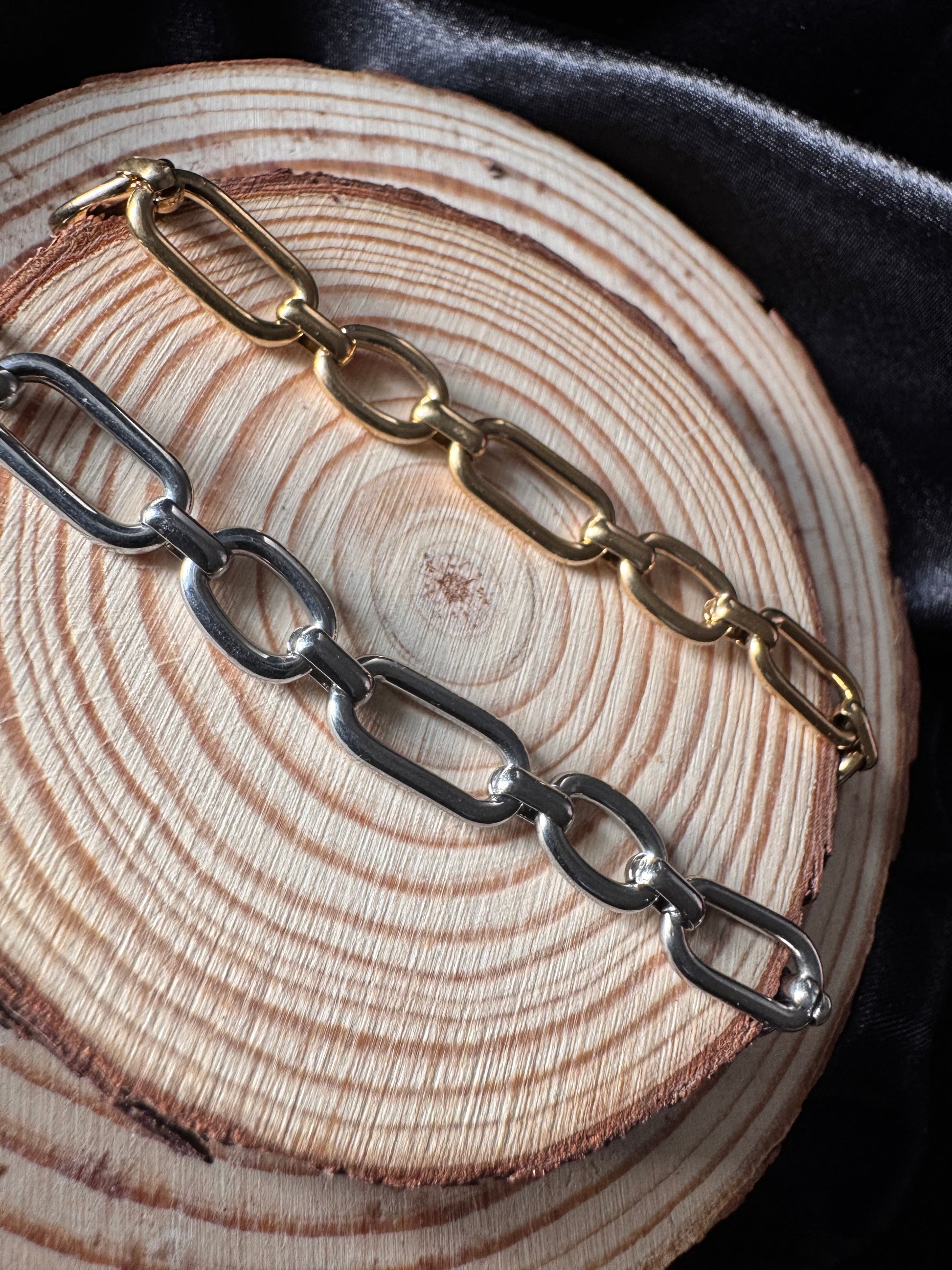 Two chain anklets, one gold and one silver, on a wooden surface.