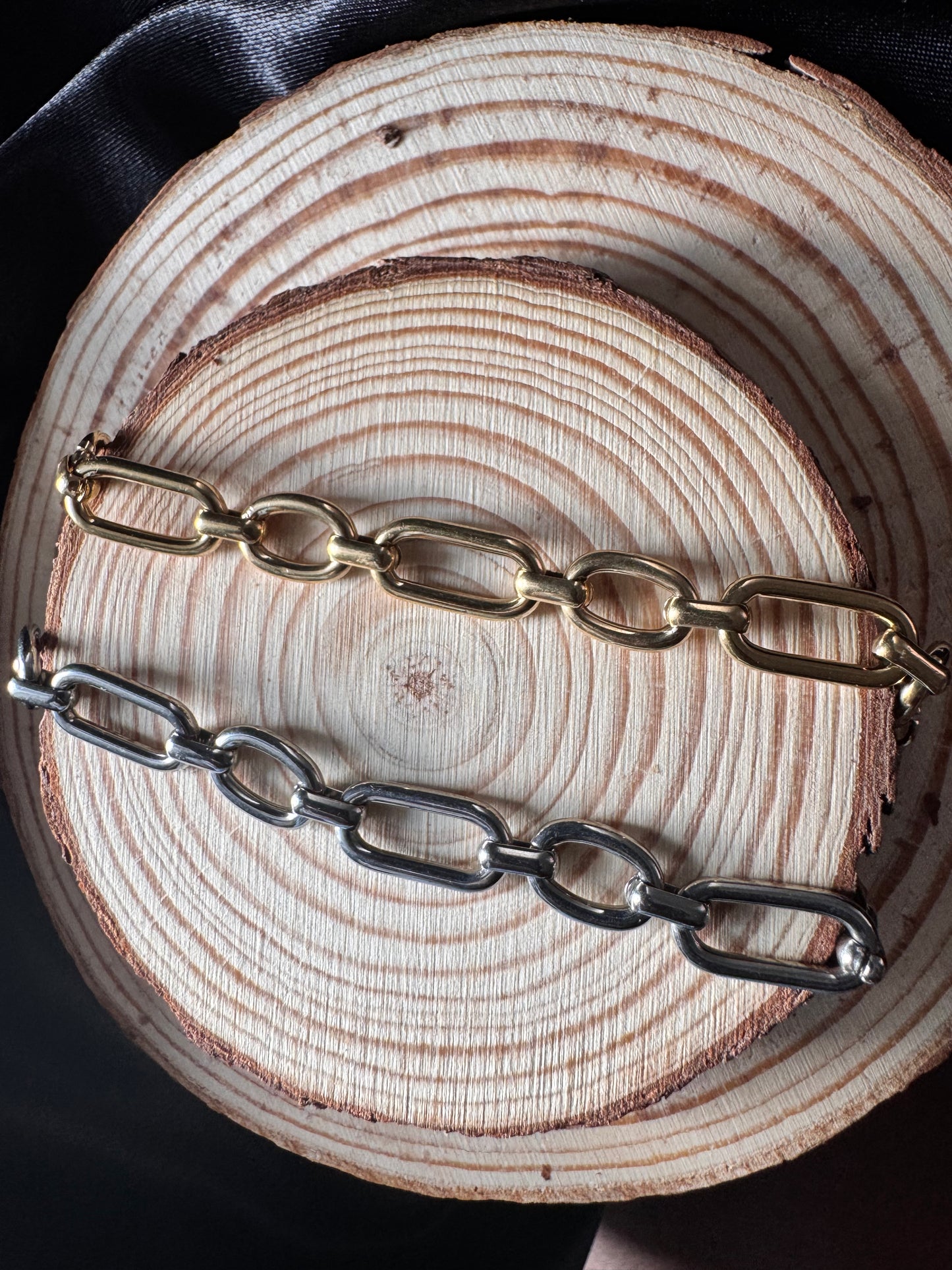 Two chain anklets one gold and one silver, on a wooden surface.
