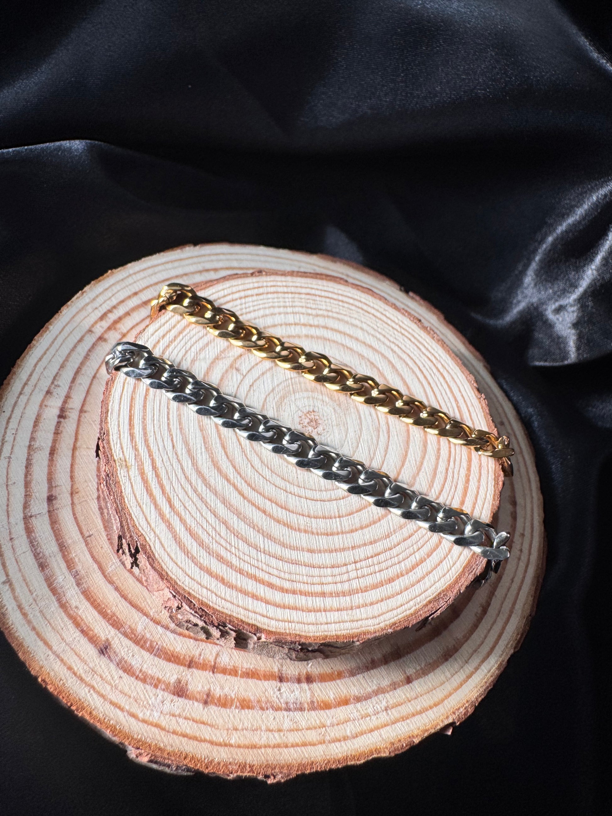 Two gold and silver chain anklets on a wooden surface with black fabric background