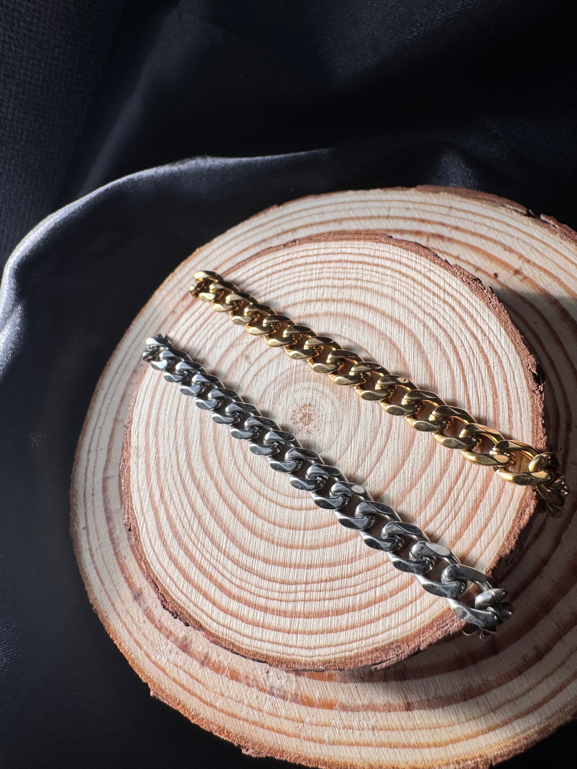 Two chain anklets, one gold and one silver, on a wooden surface.