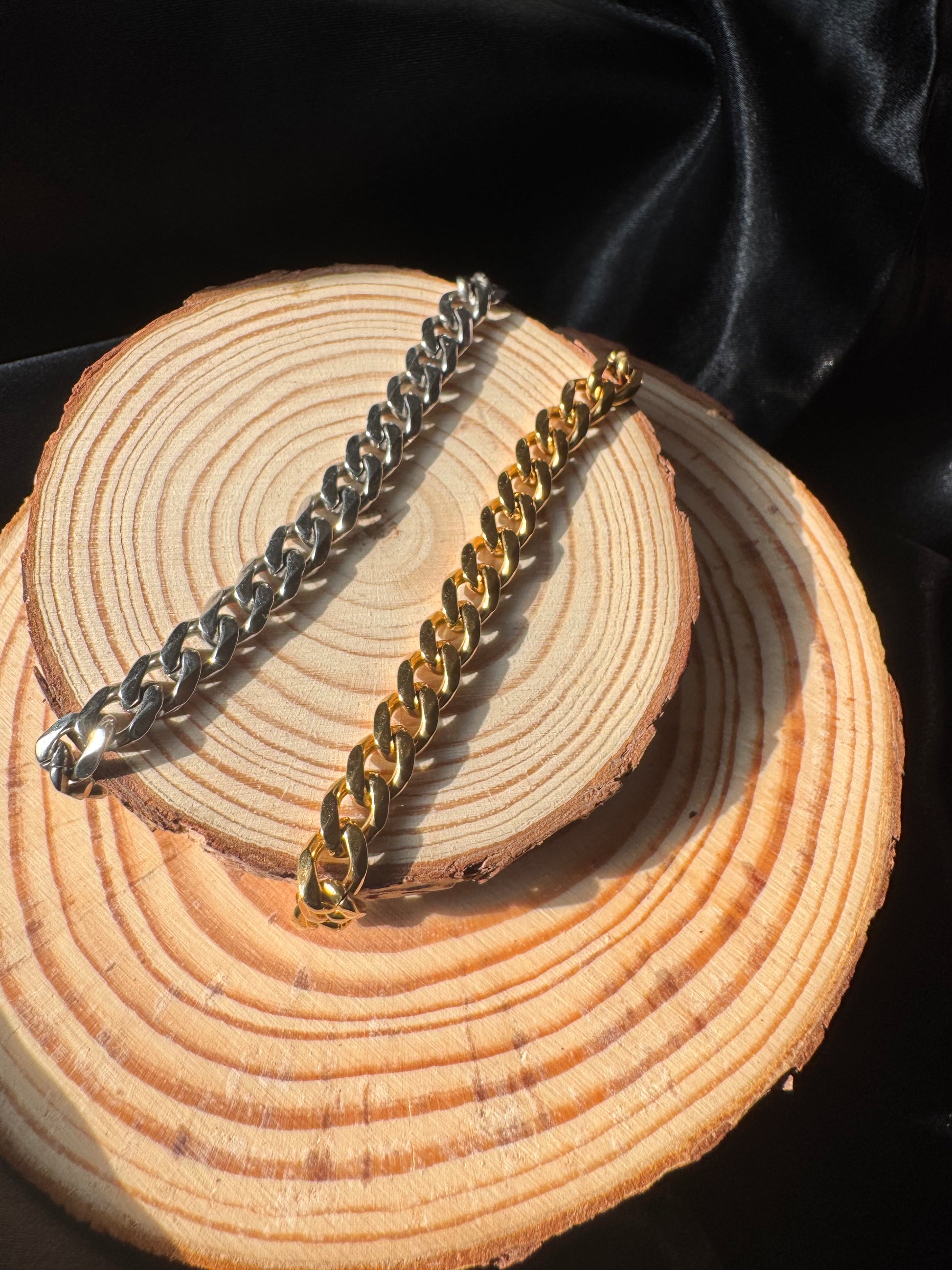 Gold and silver anklets on a wooden surface with black fabric background