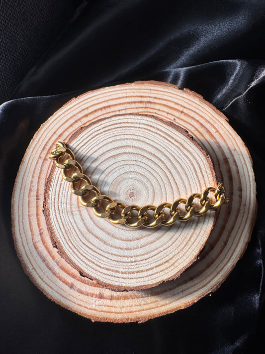 Gold chain anklet on a wooden surface with a dark background