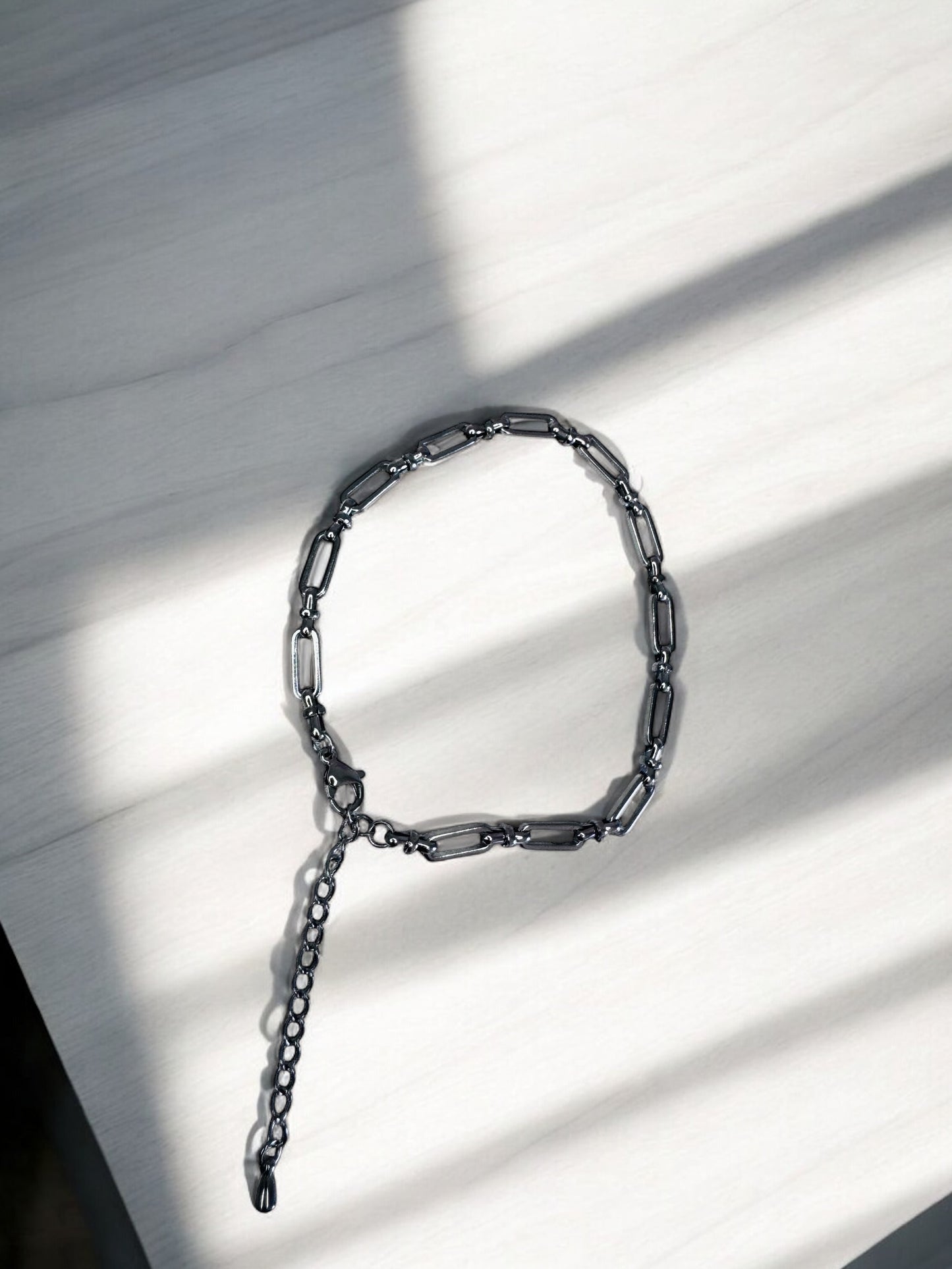 Silver bold link anklet on a light wooden surface with shadows