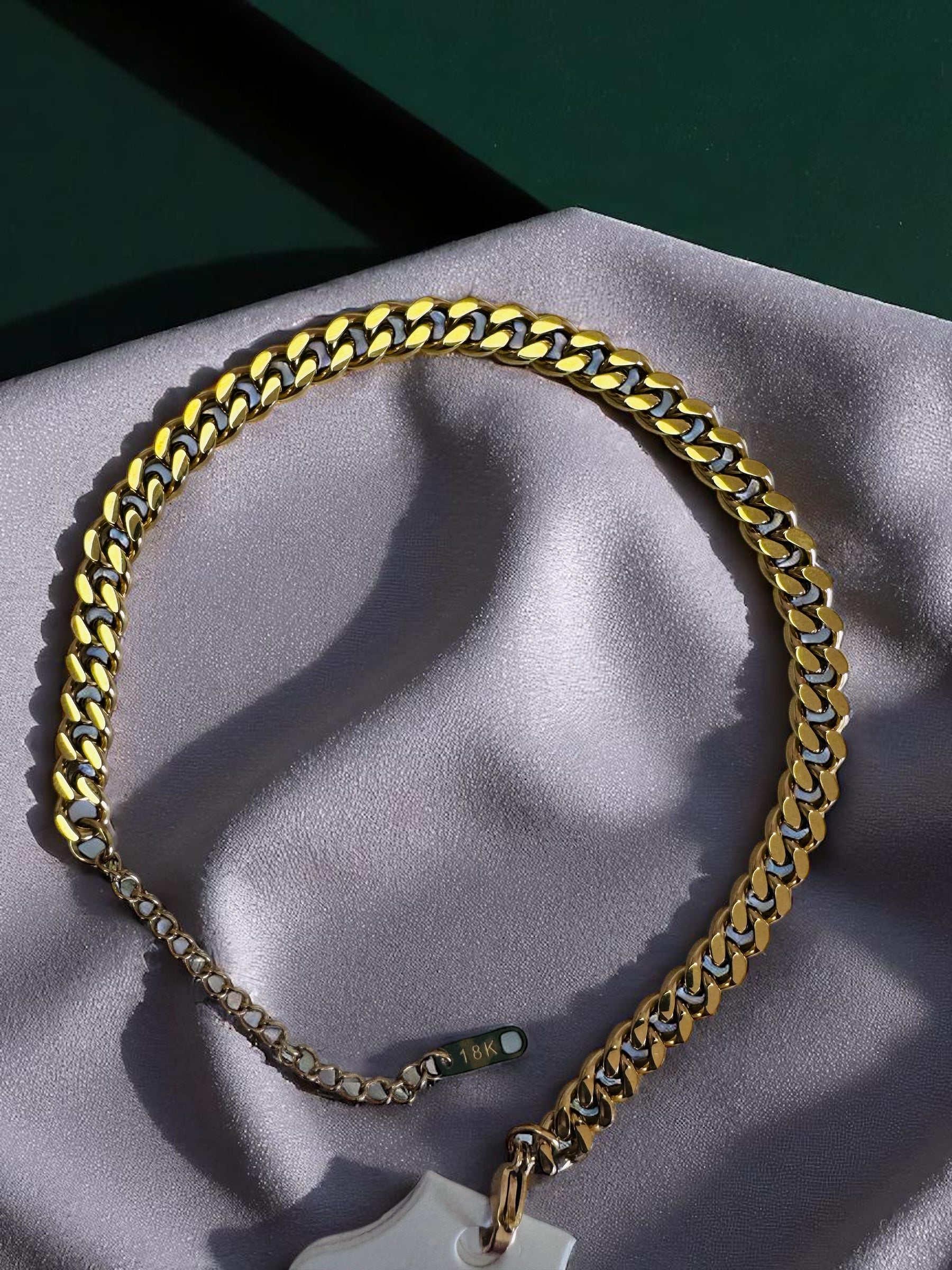 18k. cuban link anklet with a cross pendant on a gray surface